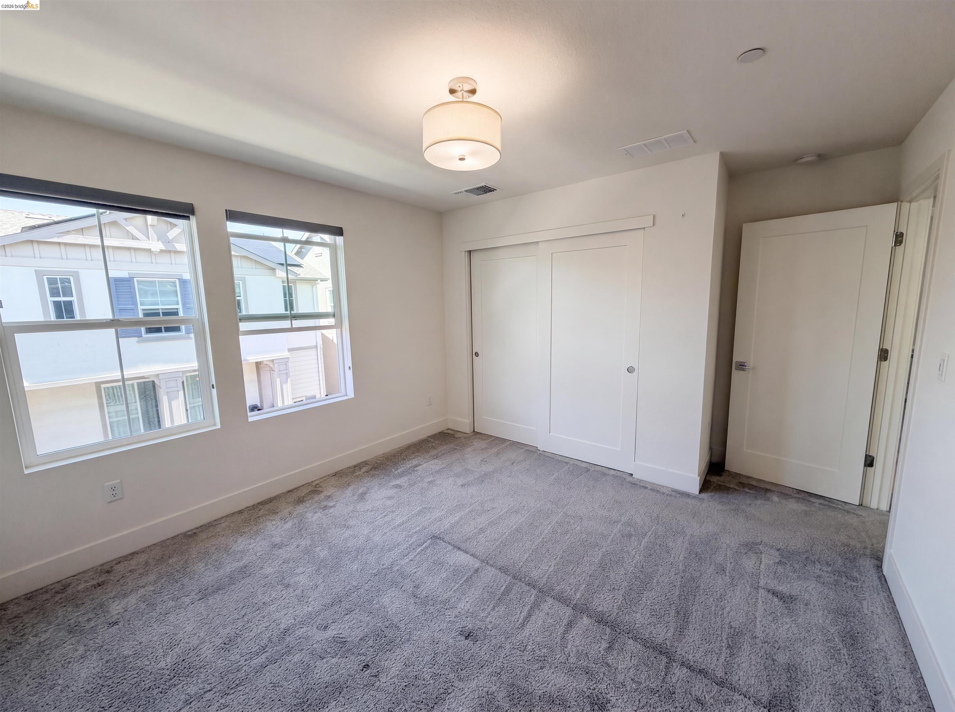 9034 Rudder Way Newark, CA 94560 - Photo 11 of 38 Bright room featuring two large windows with roller shades, light gray carpeting, and a flush-mount ceiling light fixture