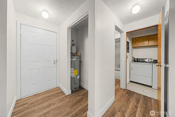 a view of a hallway to an empty room with wooden floor and a window