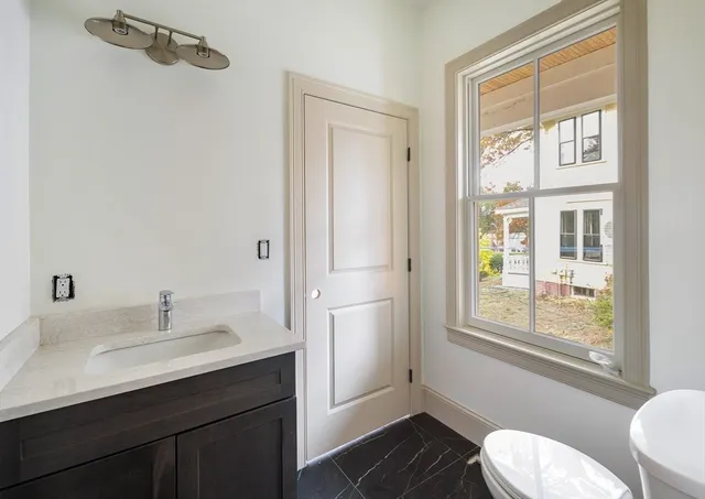 a bathroom with a sink toilet a mirror and next to a window