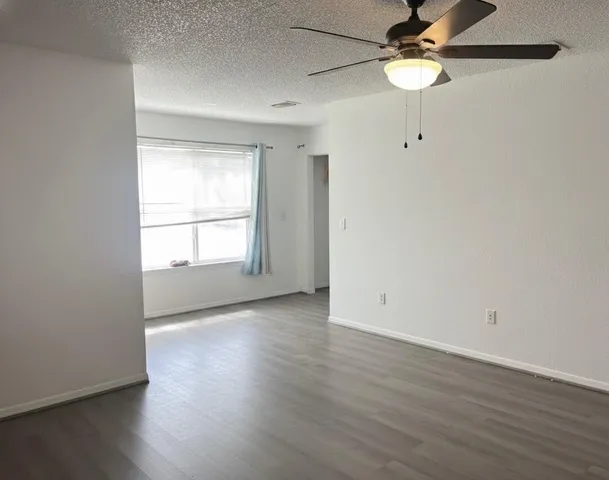 an empty room with wooden floor fan and windows