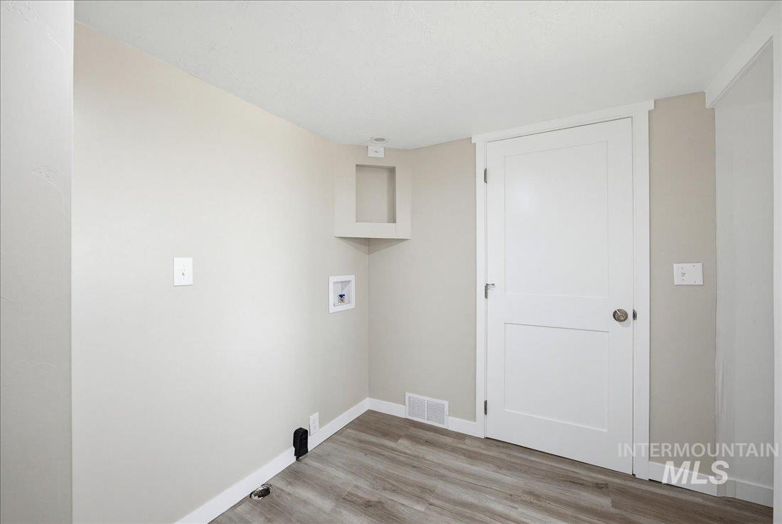 30013 Apple Valley Road Parma, ID 83660 - Photo 11 of 25 Utility area featuring wood-finish flooring, light neutral walls, and a white paneled door