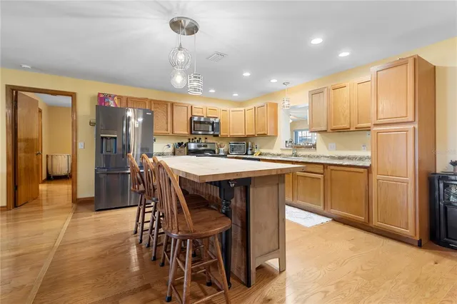 a kitchen with stainless steel appliances kitchen island granite countertop a refrigerator a stove a sink a dining table and chairs with wooden floor