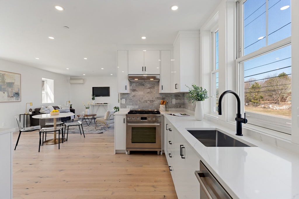 656 Mystic Avenue, Unit B Somerville, MA 02145 - Photo 13 of 40 a kitchen with stainless steel appliances a stove a sink a refrigerator and white cabinets with wooden floor