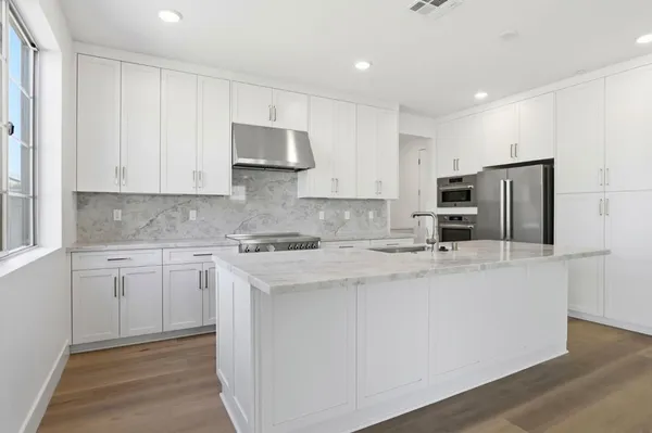 a kitchen with stainless steel appliances granite countertop a stove a sink a refrigerator and white cabinets