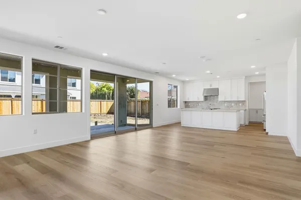 a view of an empty room with wooden floor and a kitchen