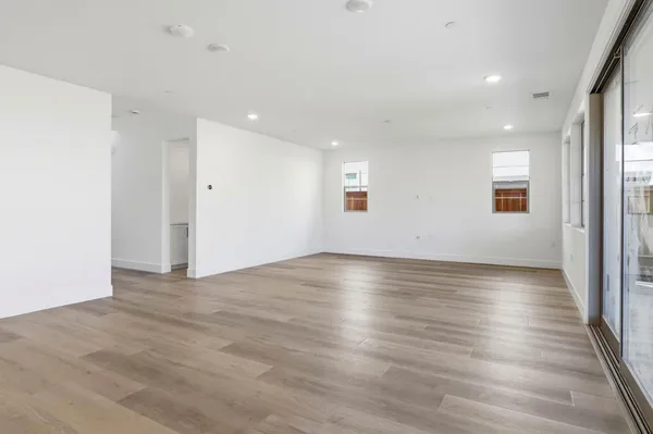 an empty room with wooden floor and windows with curtains