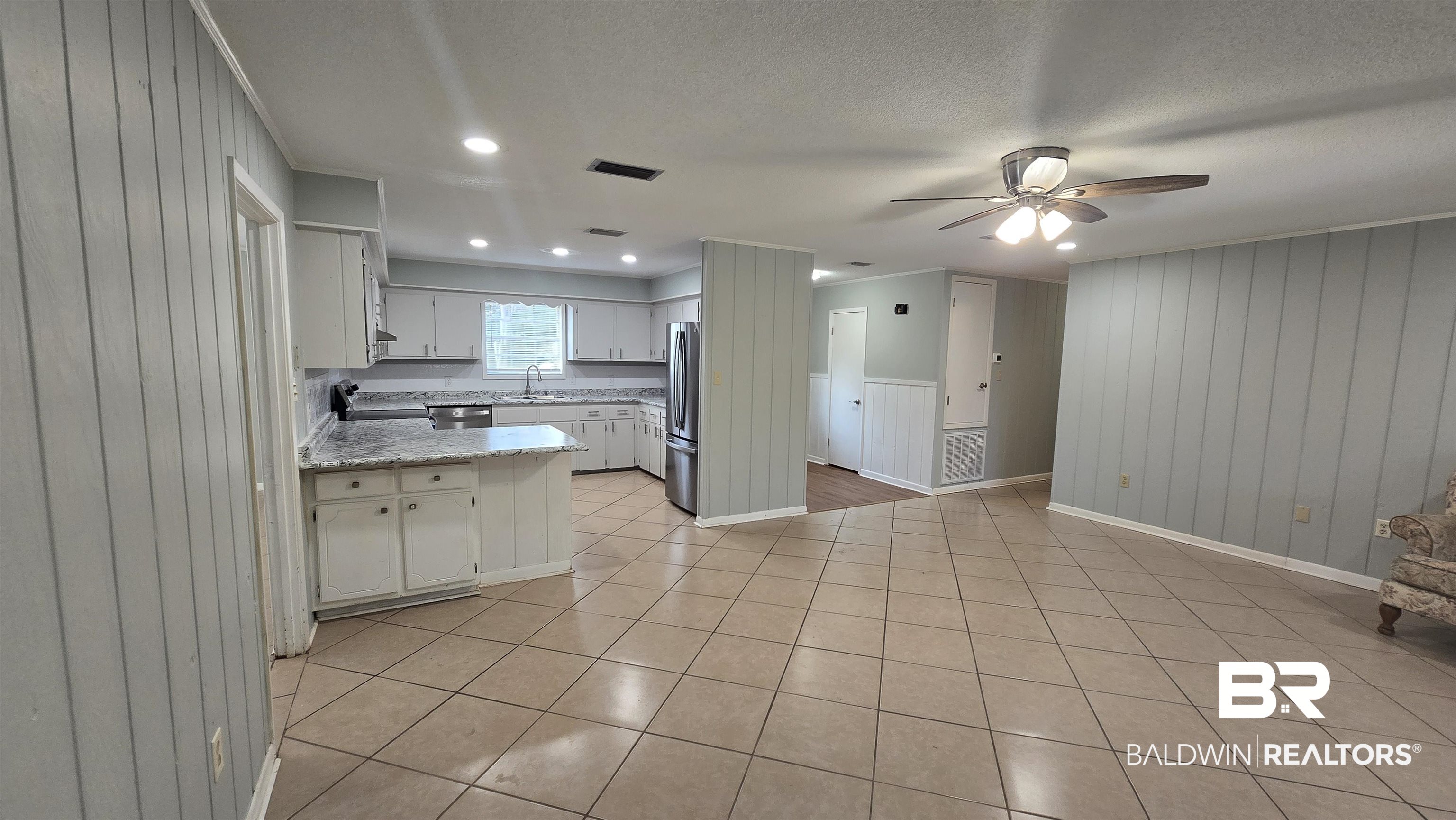 615 East Pedigo Avenue Foley, AL 36535 - Photo 12 of 31 Kitchen featuring light tile patterned flooring, white cabinetry, wooden walls, ceiling fan, and a peninsula