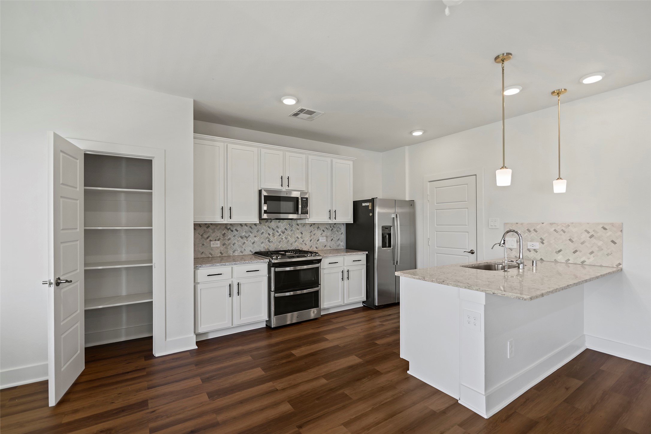 10603 Whitejacket Conroe, TX 77385 - Photo 25 of 42 This modern kitchen features sleek white cabinetry, stainless steel appliances, and a spacious island with pendant lighting. The hardwood floors and open shelving pantry add functionality and style.