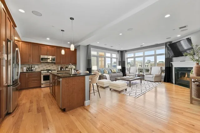 a living room with stainless steel appliances furniture wooden floor and a kitchen view
