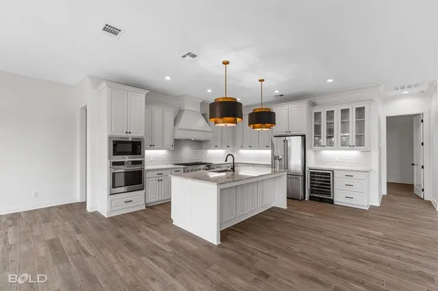 a kitchen with stainless steel appliances granite countertop a stove top oven a sink dishwasher and a refrigerator with wooden floor