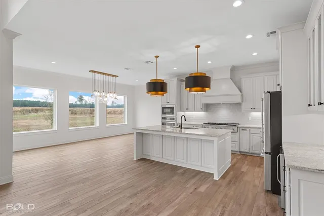 a kitchen with stainless steel appliances granite countertop a stove a sink and white cabinets with wooden floor next to windows