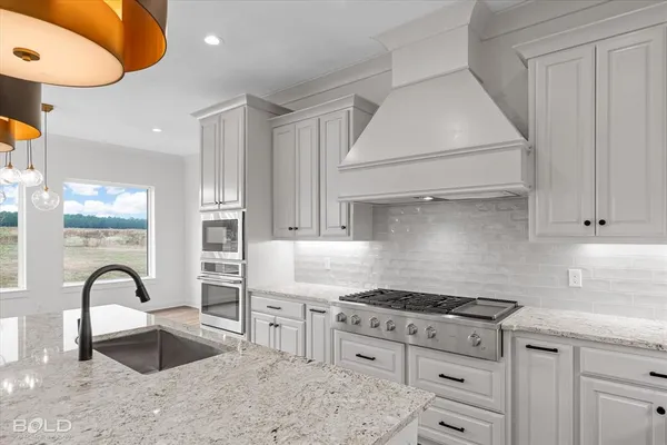 a kitchen with stainless steel appliances granite countertop a stove a sink dishwasher and white cabinets with wooden floor