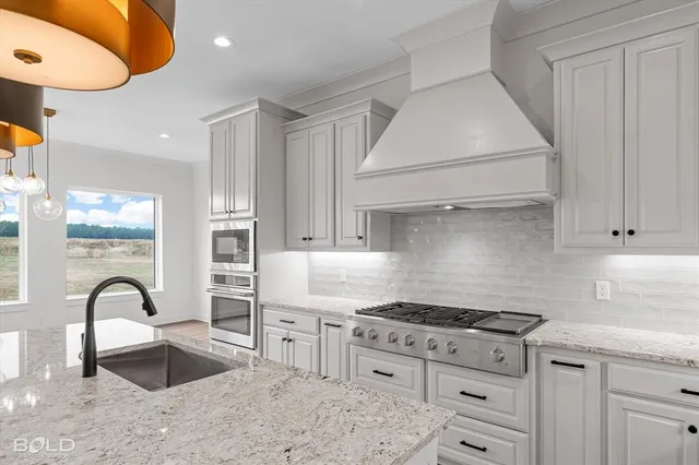 a kitchen with stainless steel appliances granite countertop a stove a sink dishwasher and white cabinets with wooden floor