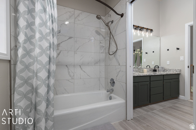 2807 North Ogden Canyon Road Eden, UT 84310 - Photo 26 of 72 Bathtub with marble-patterned tile surround, dual sink vanity with granite-patterned countertop, dark cabinetry, and wood-finish flooring