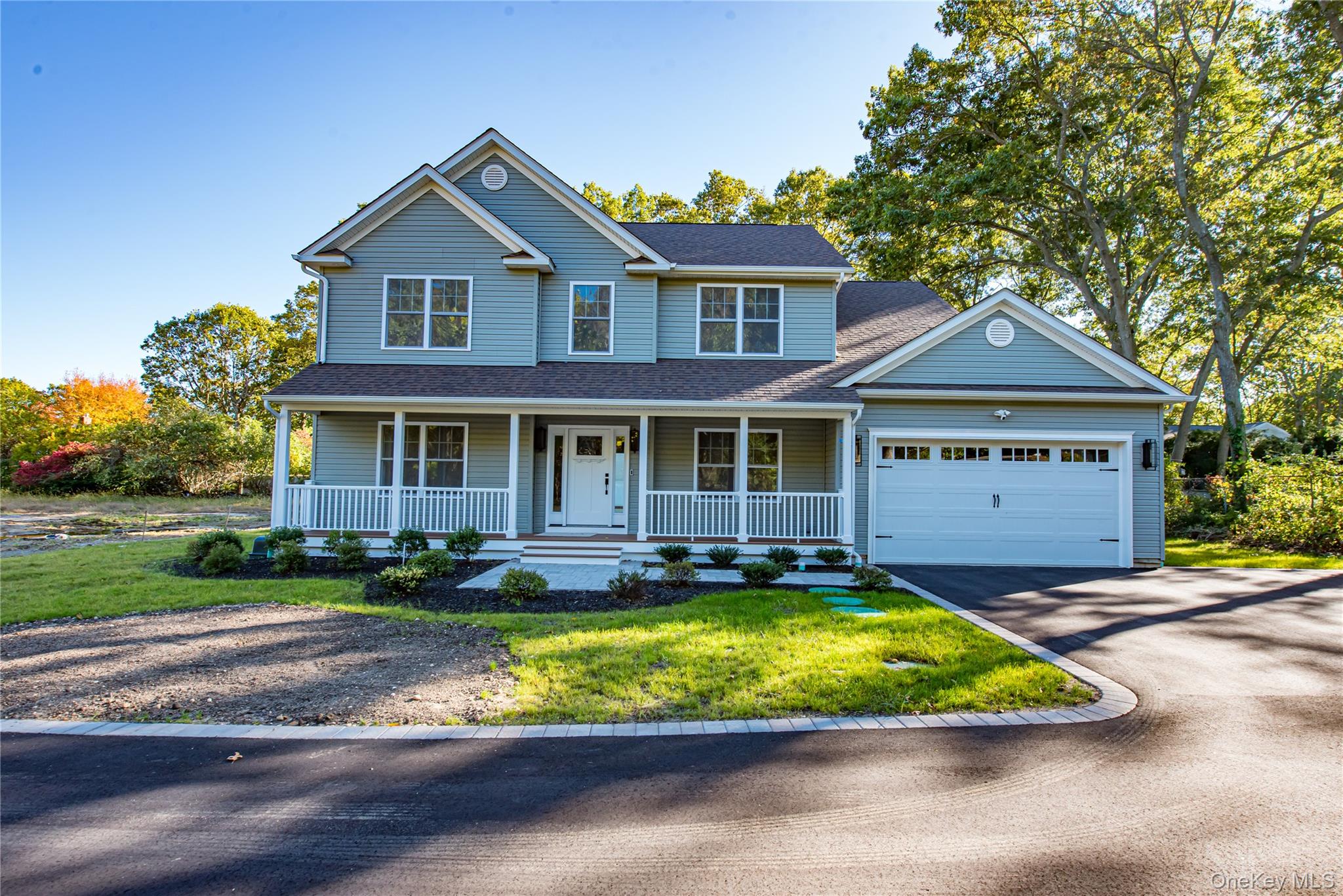 View of front facade featuring a porch, driveway, roof with shingles, a front lawn, and an attached garage