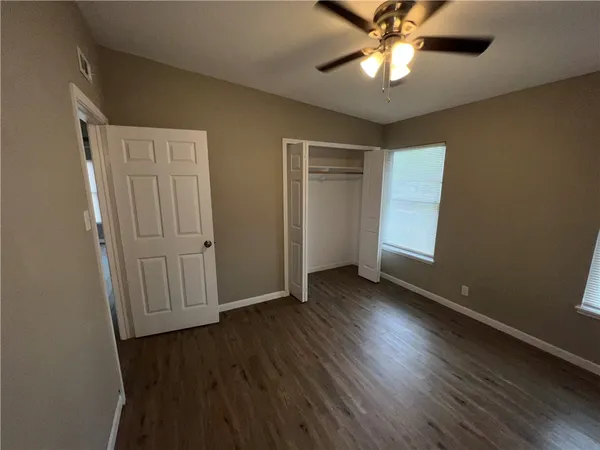 an empty room with wooden floor closet fan and windows