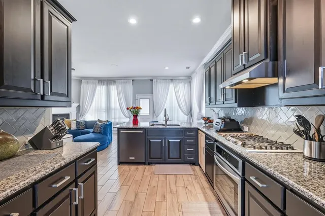 a kitchen with stainless steel appliances granite countertop a stove top oven a sink dishwasher and cabinets with wooden floor