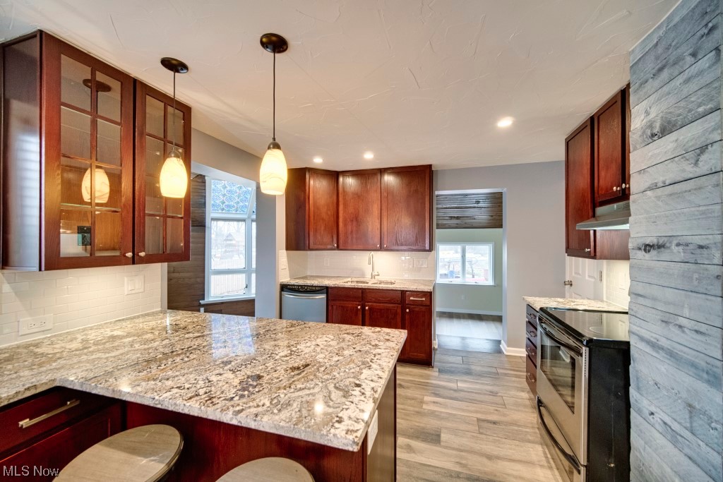 7060 Lear Nagle Road North Ridgeville, OH 44039 - Photo 18 of 29 Kitchen with wall chimney range hood, a breakfast bar, hanging light fixtures, appliances with stainless steel finishes, and light wood-type flooring