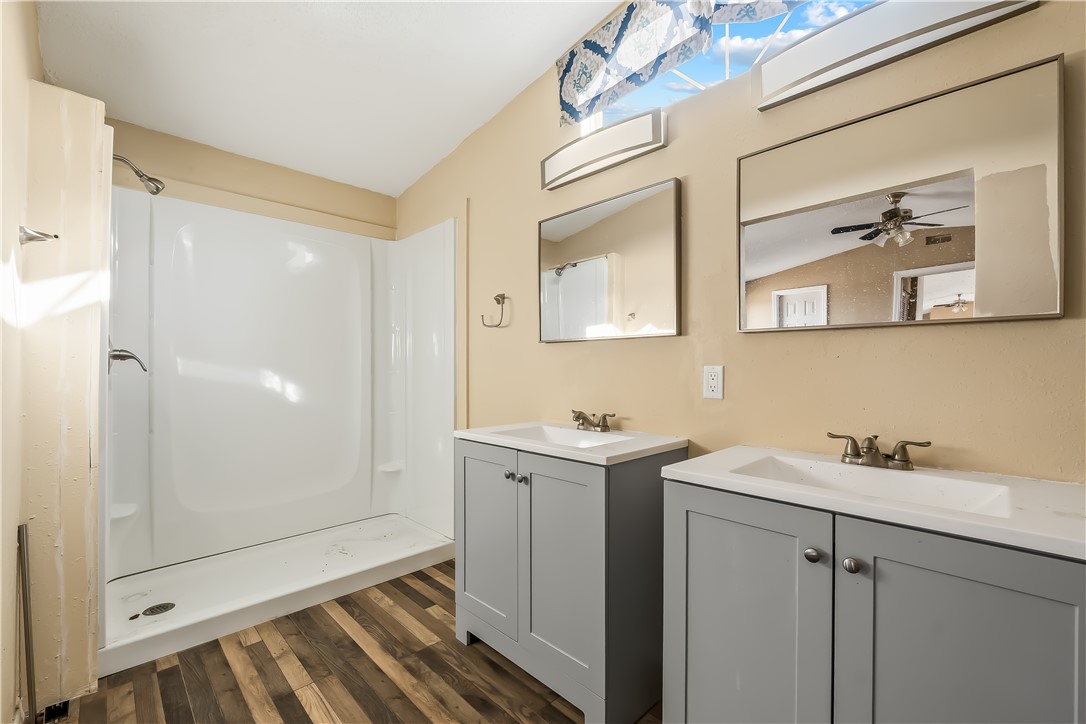 3649 Araby Road Golden Valley, AZ 86413 - Photo 23 of 29 Bathroom featuring dual grey vanity cabinets with integrated white sinks, wood-finish flooring, a white stand-up shower, and a high clerestory window