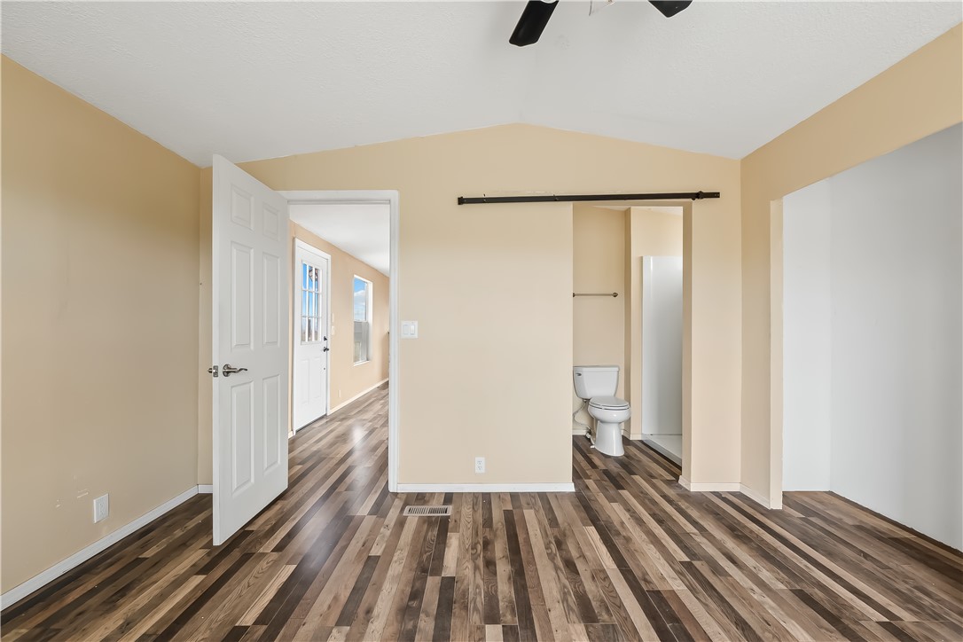 3649 Araby Road Golden Valley, AZ 86413 - Photo 6 of 29 Vaulted ceiling bedroom featuring wood-finish flooring, a ceiling fan, and a barn door entry to a three-piece bathroom with a shower
