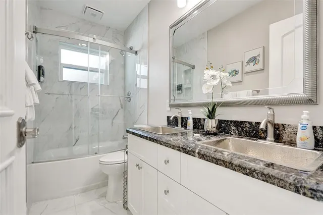 a bathroom with a granite countertop bathtub sink vanity mirror and toilet