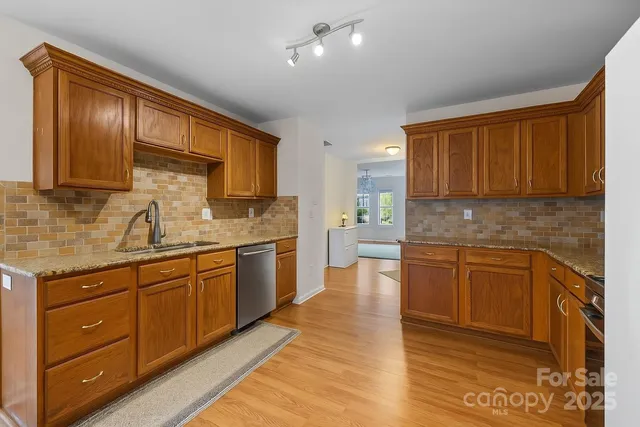 a kitchen with stainless steel appliances granite countertop a stove top oven a sink dishwasher a dining table and chairs with wooden floor