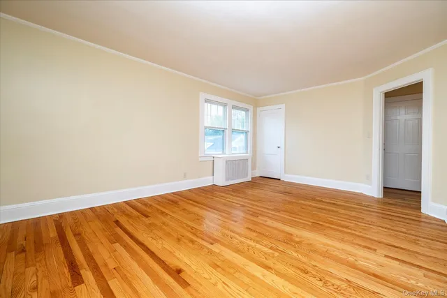a view of an empty room with wooden floor and window