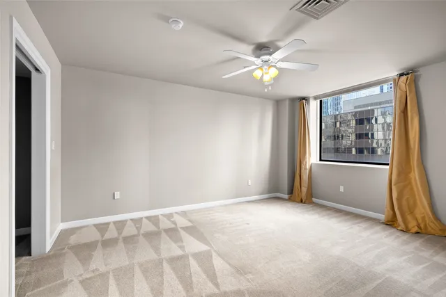 a view of an empty room with window and chandelier fan