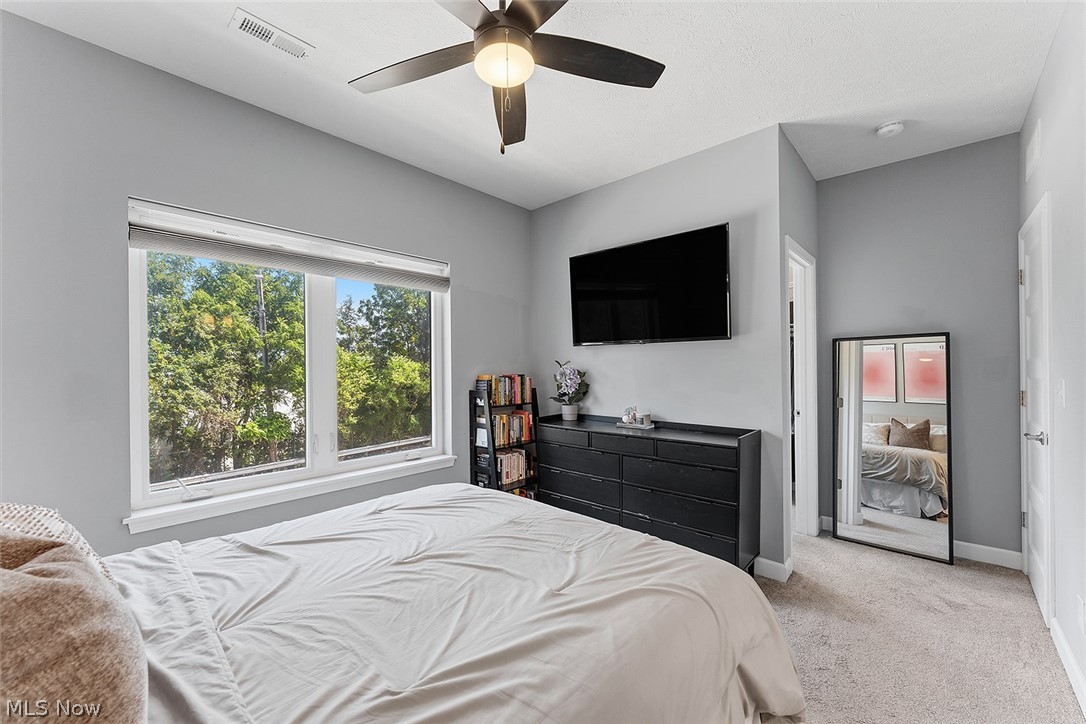 2308 Fulton Road Cleveland, OH 44113 - Photo 17 of 30 Window featuring treetop scenery, ceiling fan with integrated lighting, wall-mounted television, and neutral-toned carpeting