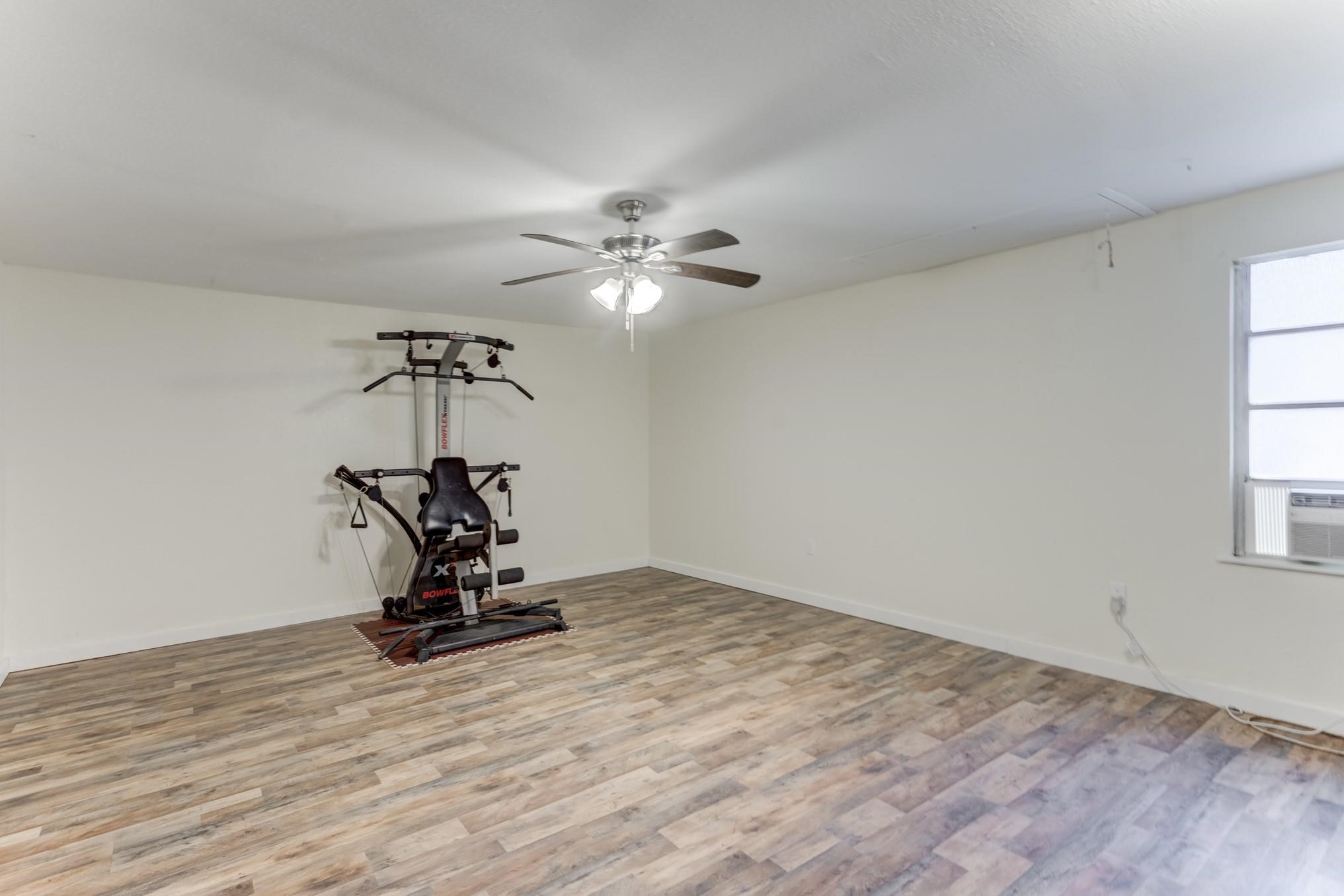 305 Yaupon Street Sweeny, TX 77480 - Photo 6 of 22 This spacious room features wood-look flooring, neutral walls, and a ceiling fan. It includes a home gym setup, ideal for fitness enthusiasts, and a window that allows natural light to brighten the space.