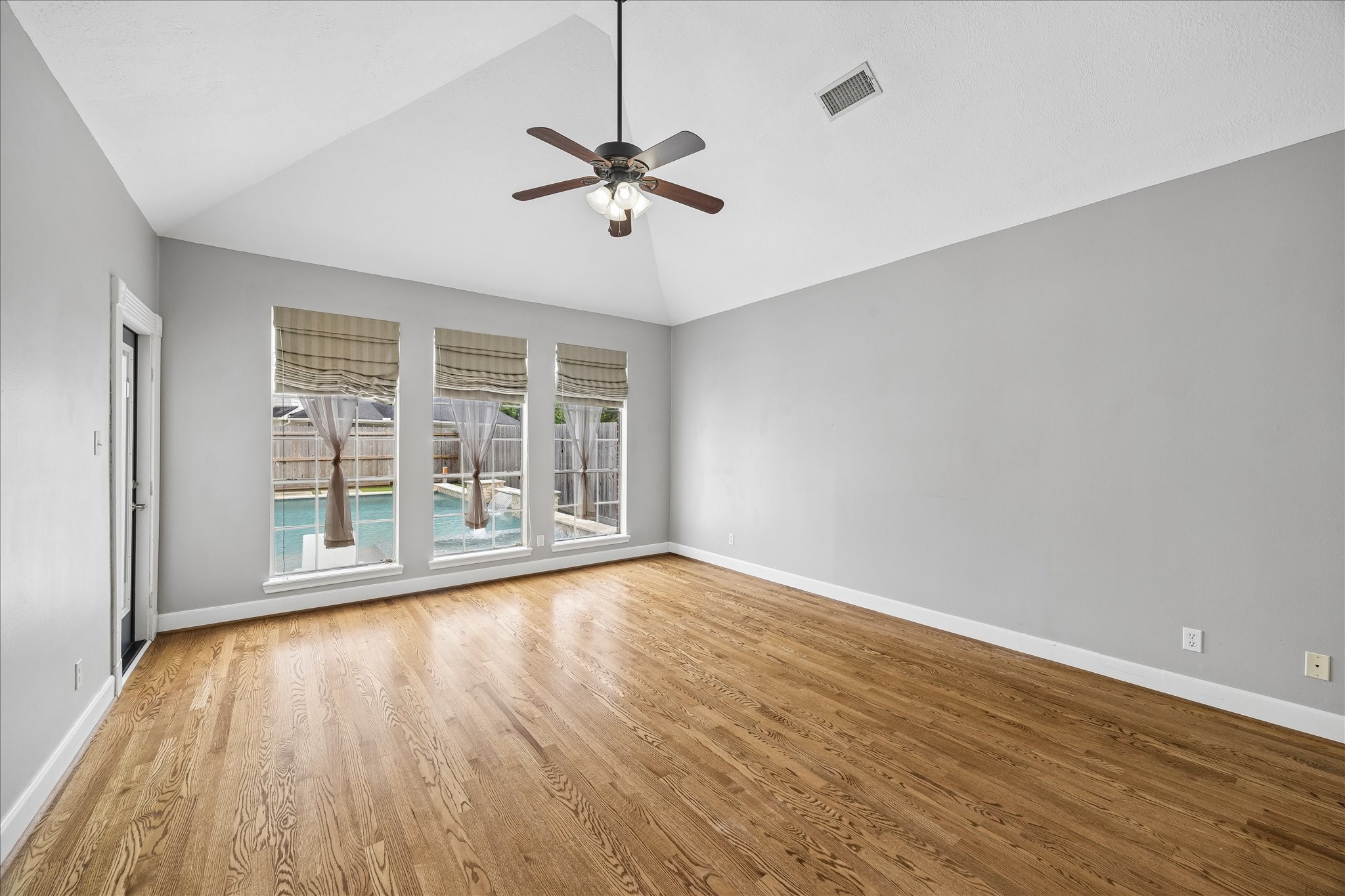 7915 Huddersfield Court Spring, TX 77379 - Photo 8 of 37 First-floor primary bedroom with vaulted ceiling, hardwood floors, backyard access, and tall windows overlooking the pool.