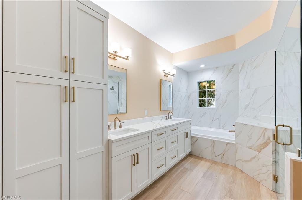 23151 Rosedale Drive, Unit 101 Estero, FL 34135 - Photo 15 of 20 Primary bathroom with new cabinets, mirrors, lighting, bathtub, and frameless shower enclosure.