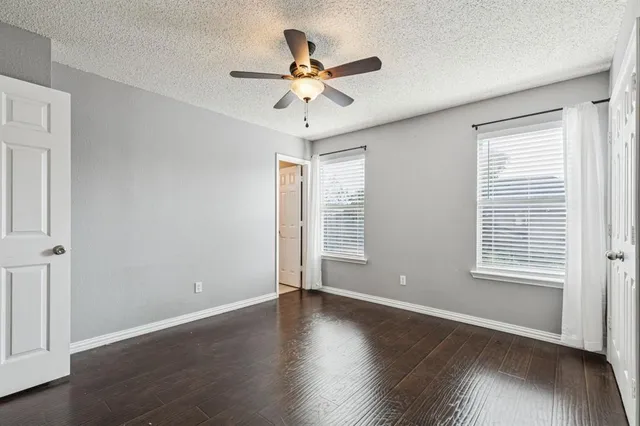 an empty room with wooden floor fan and windows