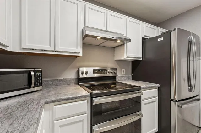 a kitchen with stainless steel appliances granite countertop white cabinets and a stove top oven