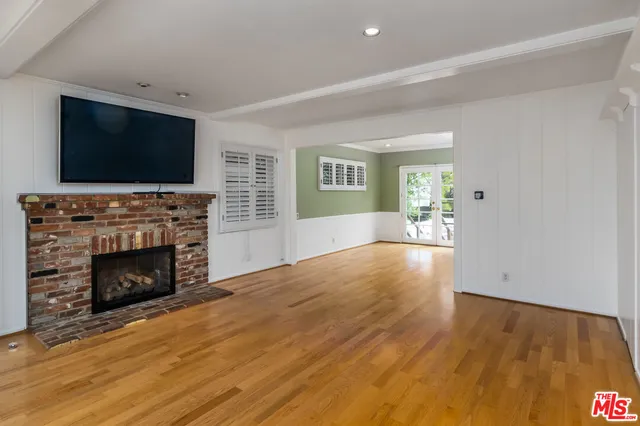 a view of an empty room with wooden floor fireplace and a window