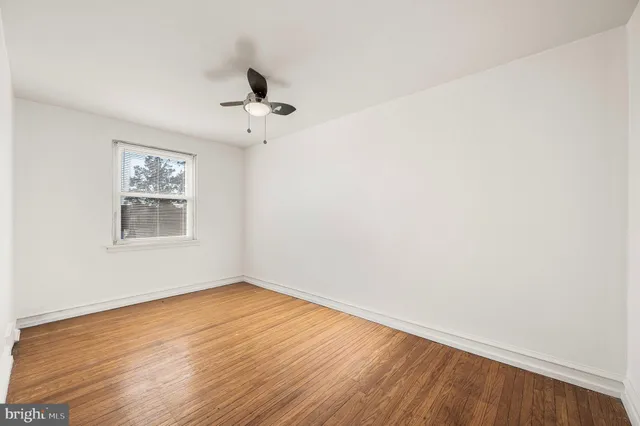 an empty room with wooden floor ceiling fan and windows