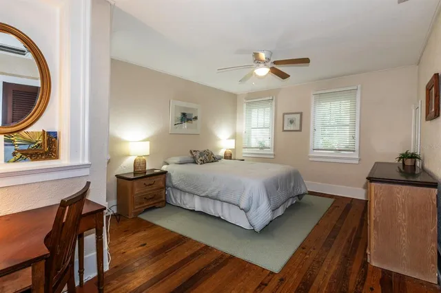 a bedroom with a bed a dresser and potted plants with the wooden floor