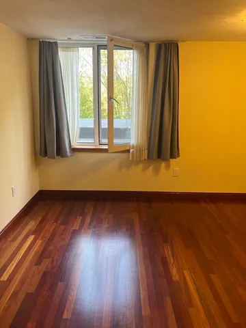 a view of an empty room with wooden floor and a window