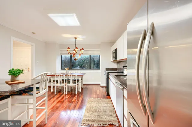 a kitchen with stainless steel appliances granite countertop a refrigerator a stove top oven a dining table and chairs with wooden floor