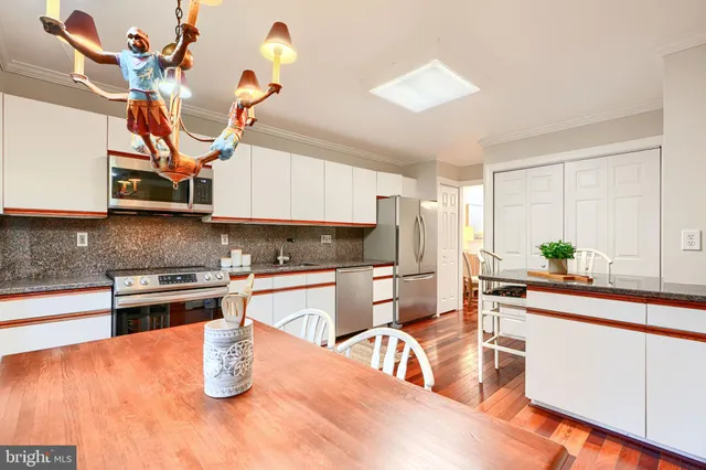 a kitchen with stainless steel appliances granite countertop a sink a stove a dining table and chairs with wooden floor