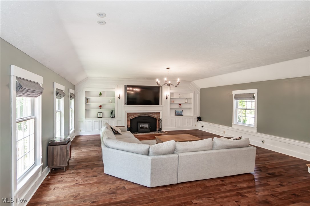7806 Fairidge Road Willoughby, OH 44094 - Photo 24 of 41 Living area featuring built in features, a chandelier, a fireplace, lofted ceiling, and dark wood-style flooring