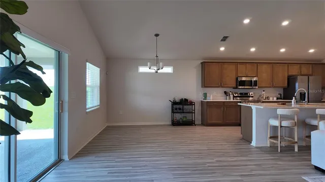 a kitchen with stainless steel appliances granite countertop a refrigerator a sink dishwasher a stove and a dining table with wooden floor