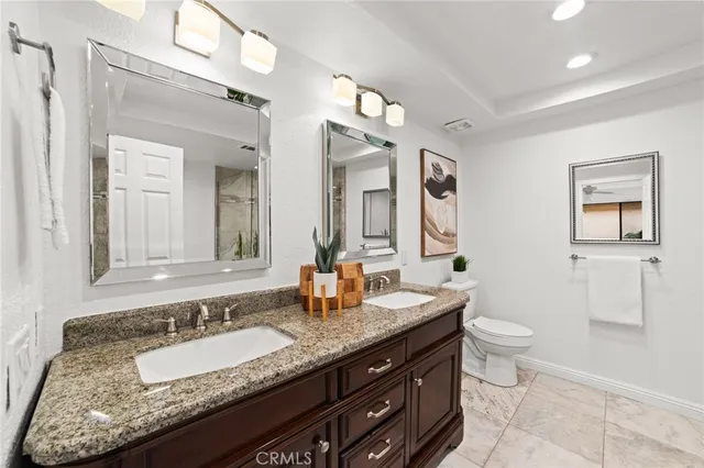 a bathroom with a granite countertop double vanity sink mirror and toilet