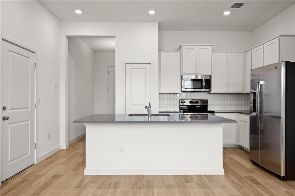 15004 Ryman Road Austin, TX 78660 - Photo 2 of 23 Kitchen featuring appliances with stainless steel finishes, white cabinets, tasteful backsplash, a center island with sink, and light wood finished floors
