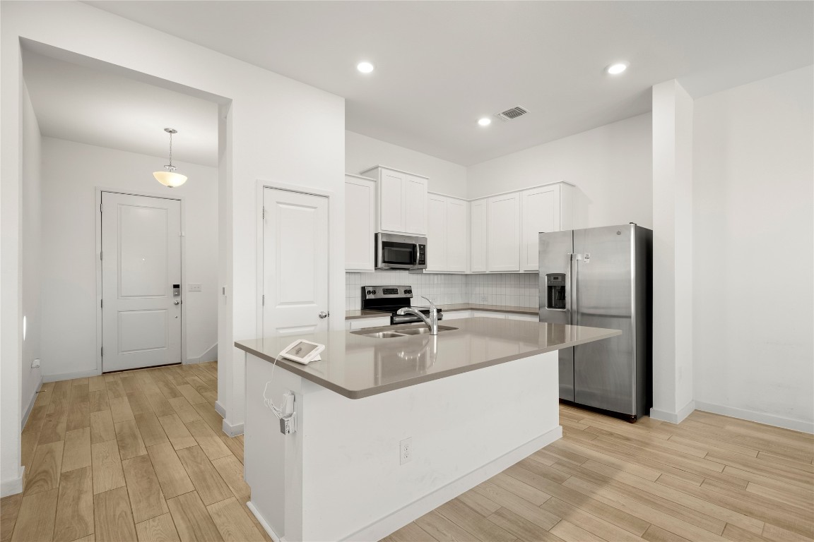 15004 Ryman Road Austin, TX 78660 - Photo 3 of 23 Kitchen with appliances with stainless steel finishes, white cabinetry, an island with sink, light wood-type flooring, and recessed lighting