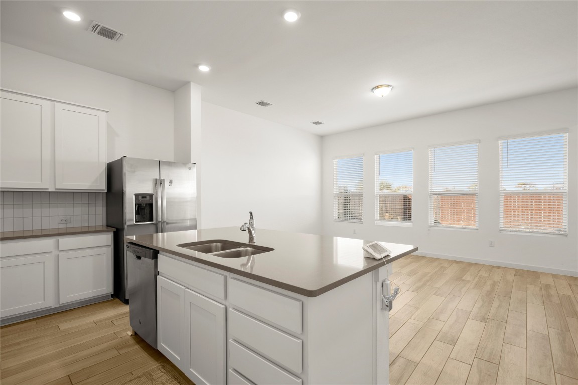 15004 Ryman Road Austin, TX 78660 - Photo 4 of 23 Kitchen featuring white cabinets, wood finish floors, a kitchen island with sink, tasteful backsplash, and recessed lighting