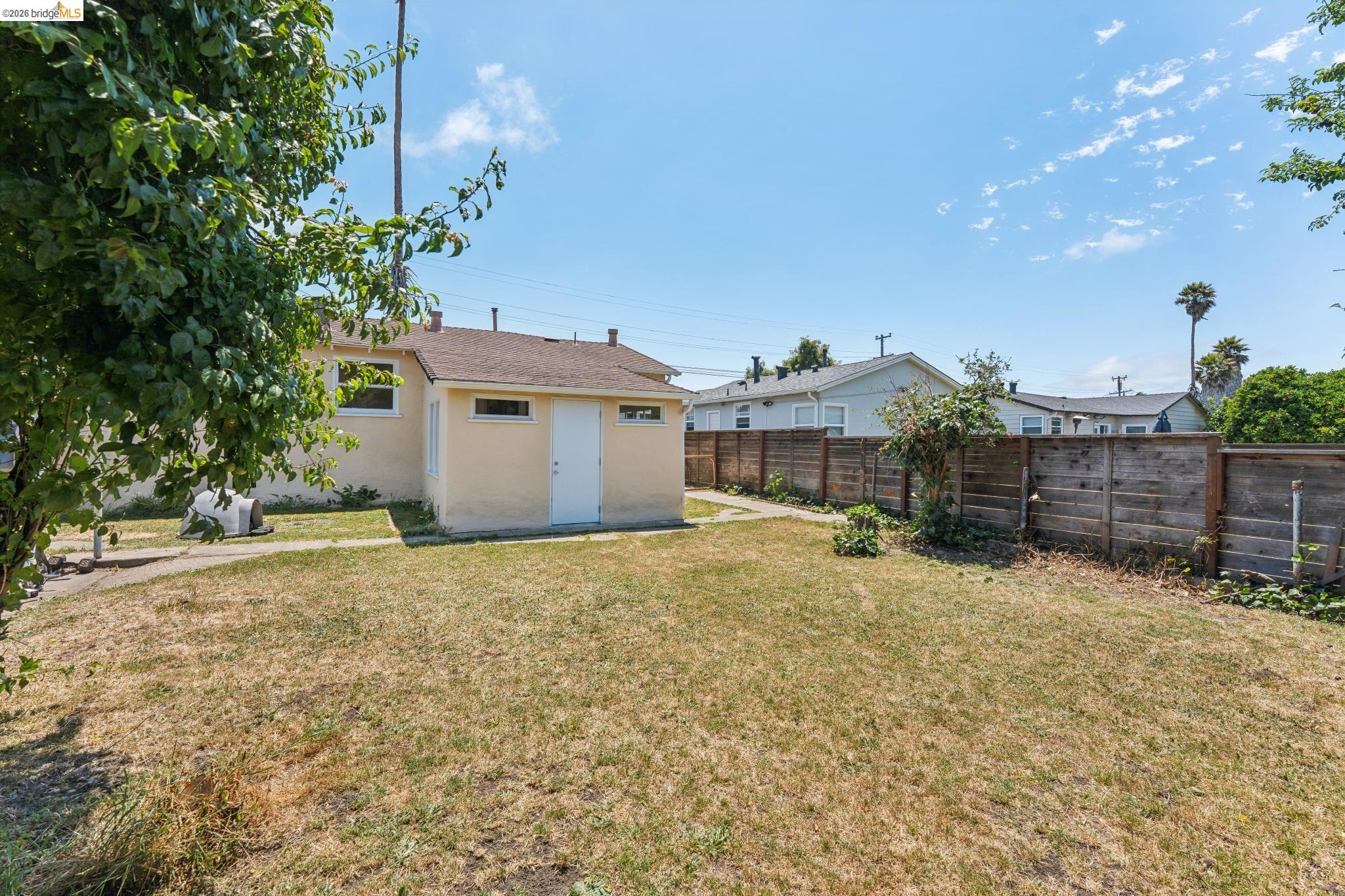 2879 Rheem Avenue Richmond, CA 94804 - Photo 38 of 45 Expansive backyard featuring a detached accessory structure with a white door, a manicured lawn, and a perimeter wood fence