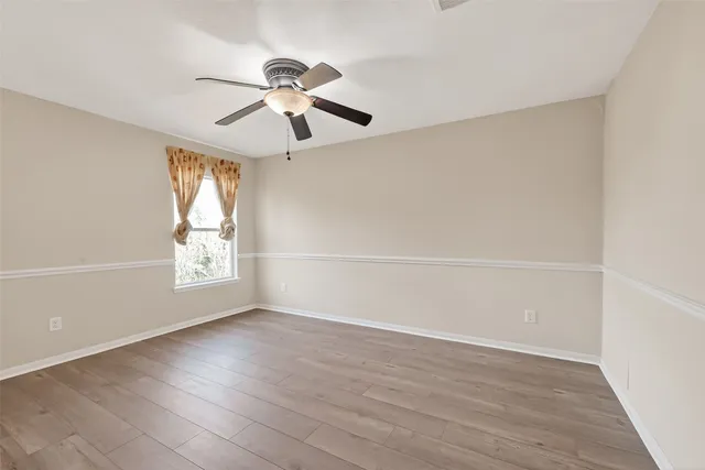 an empty room with wooden floor ceiling fan and windows