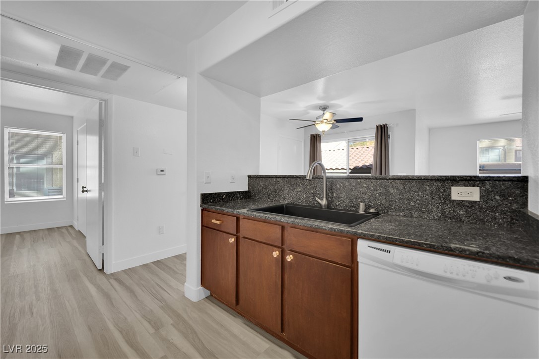 2300 East Silverado Ranch Boulevard, Unit 1189 Las Vegas, NV 89123 - Photo 13 of 27 Kitchen featuring white dishwasher, dark stone counters, light wood-style floors, brown cabinetry, and a ceiling fan