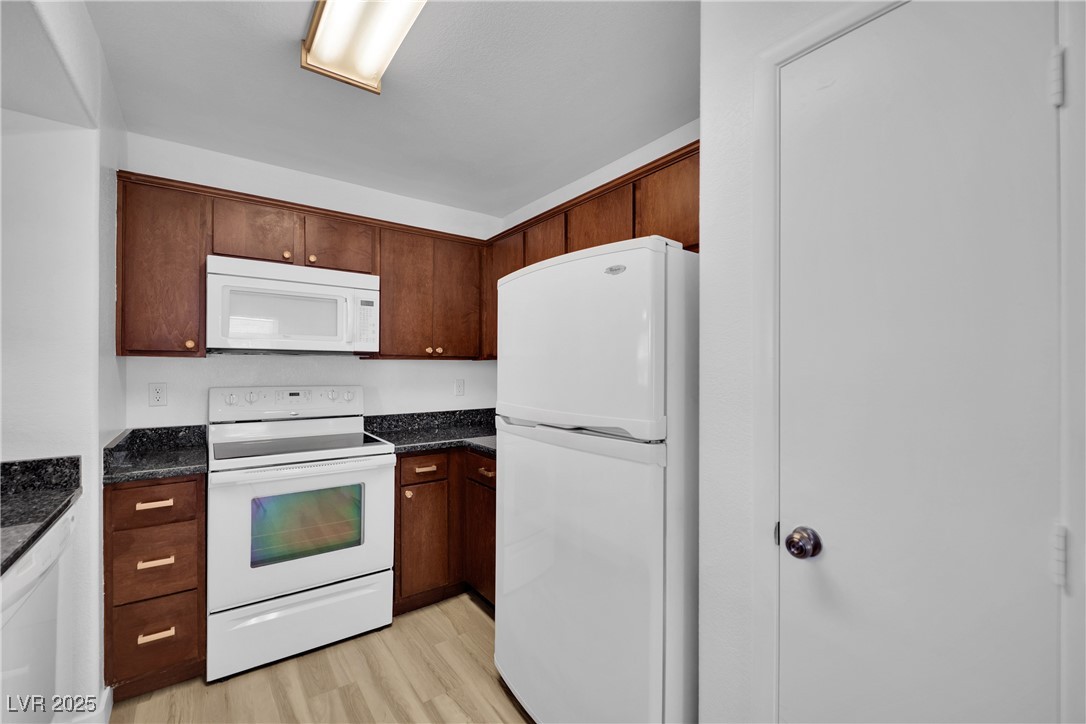 2300 East Silverado Ranch Boulevard, Unit 1189 Las Vegas, NV 89123 - Photo 15 of 27 Kitchen featuring white appliances, light wood-type flooring, dark stone countertops, and dark brown cabinetry